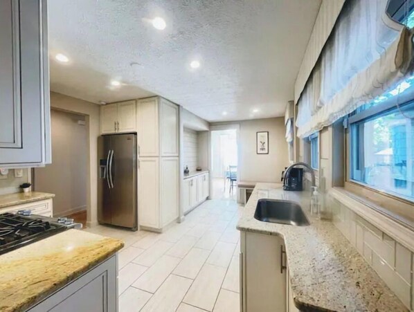 Enjoy cooking in this well-equipped kitchen with a central island, stainless steel appliances, and a large window offering a view of the outdoors.