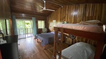 Eine Holzhütte mit Holzwänden und -böden, zwei Stockbetten, einem Deckenventilator und einem großen Fenster mit Vorhängen.