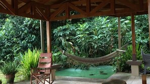 Une terrasse couverte avec un plafond en bois, un luminaire suspendu, un hamac, un banc en bois et des plantes en pot.