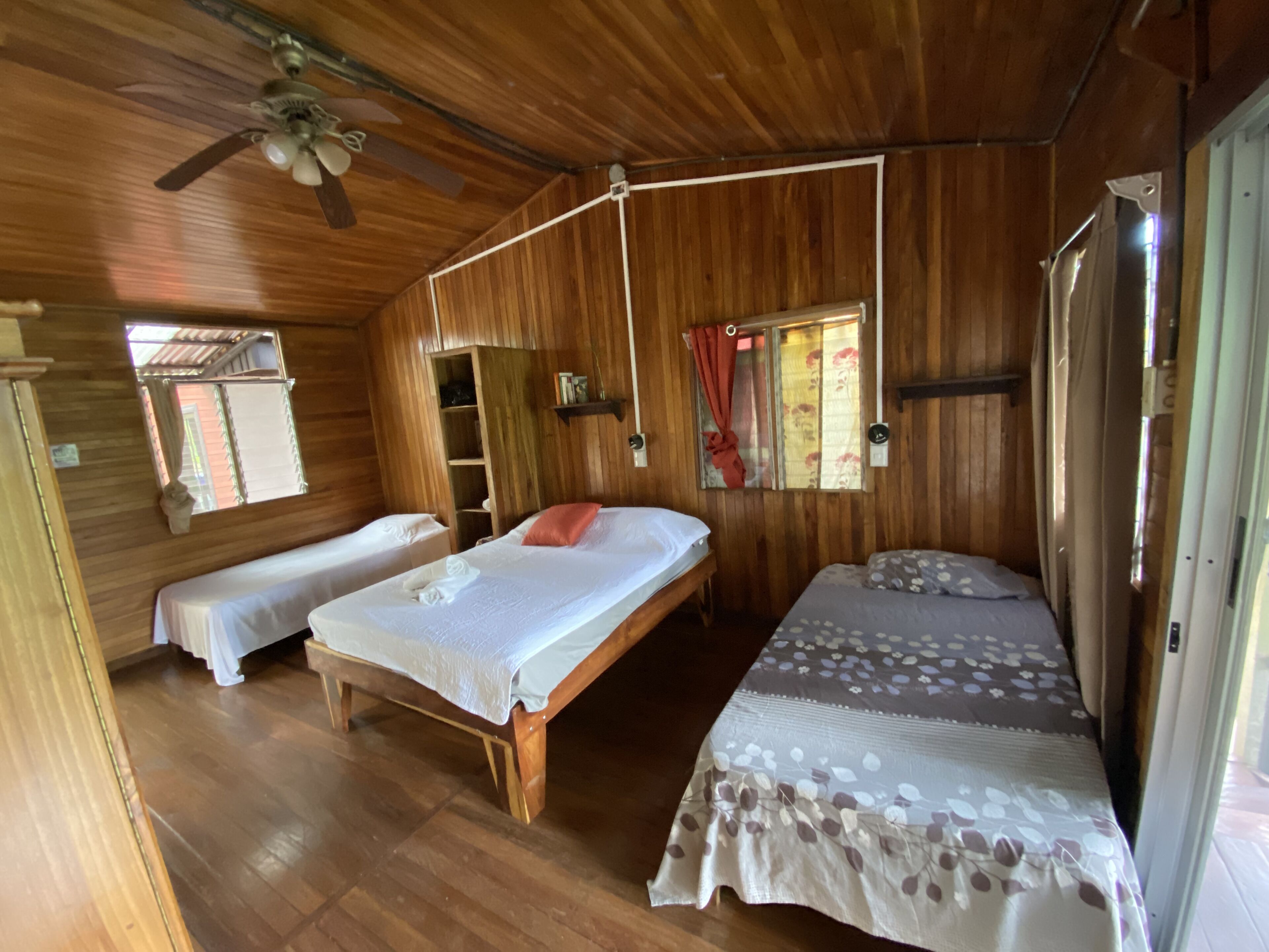 Una habitación de cabaña de madera con dos camas individuales, un ventilador de techo y una ventana con cortinas.