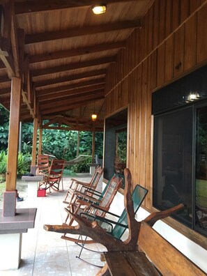A covered outdoor seating area with wooden furniture and a view of greenery. - Birds & Breakfast  (La Tigra)