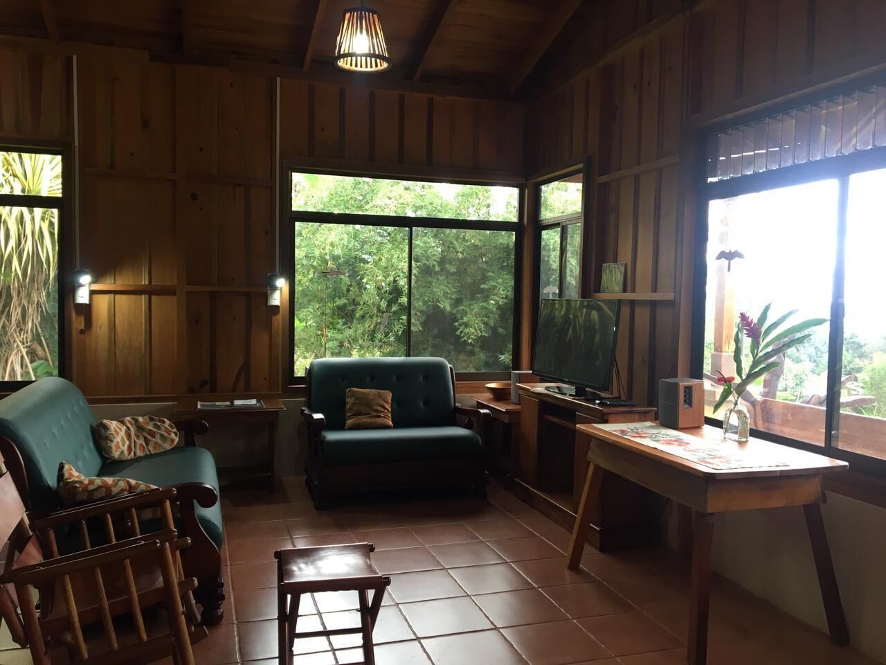 A cozy room with wooden walls, a green sofa, a wooden chair, a small table, and a TV.