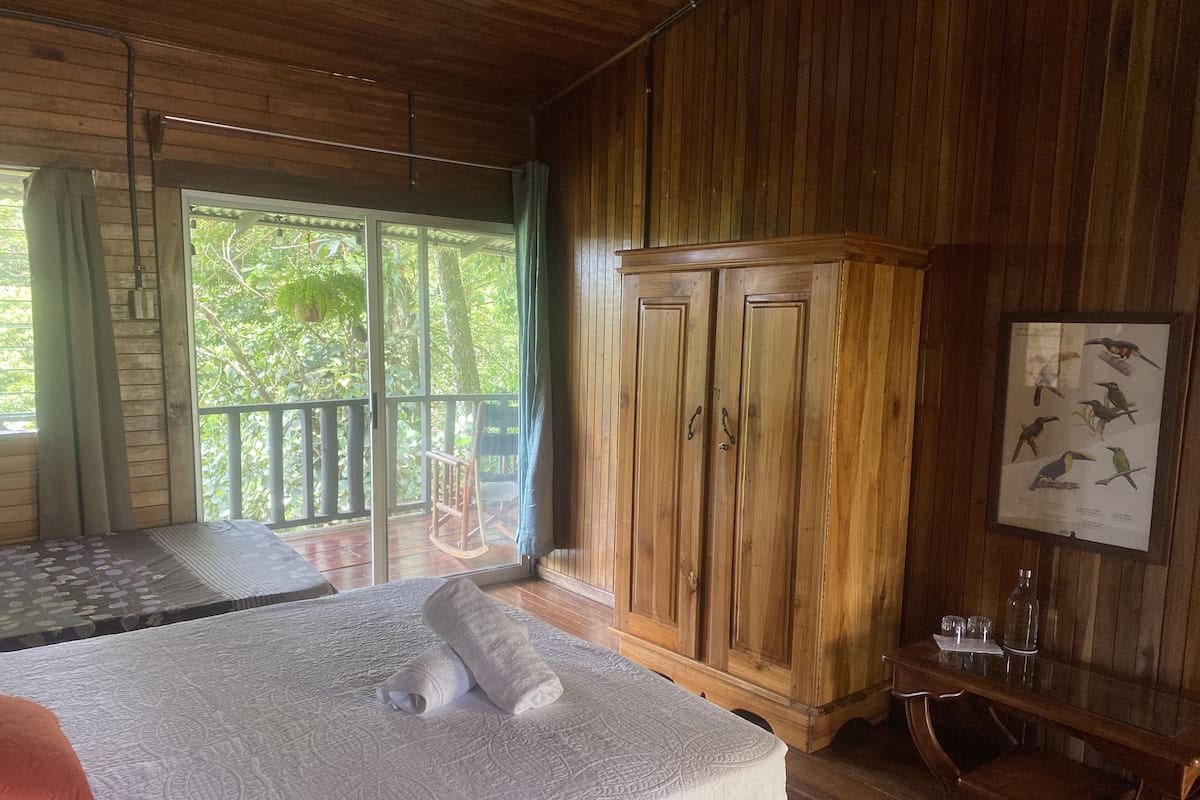 A wooden-paneled room with a bed, a wooden wardrobe, and a framed bird illustration on the wall.