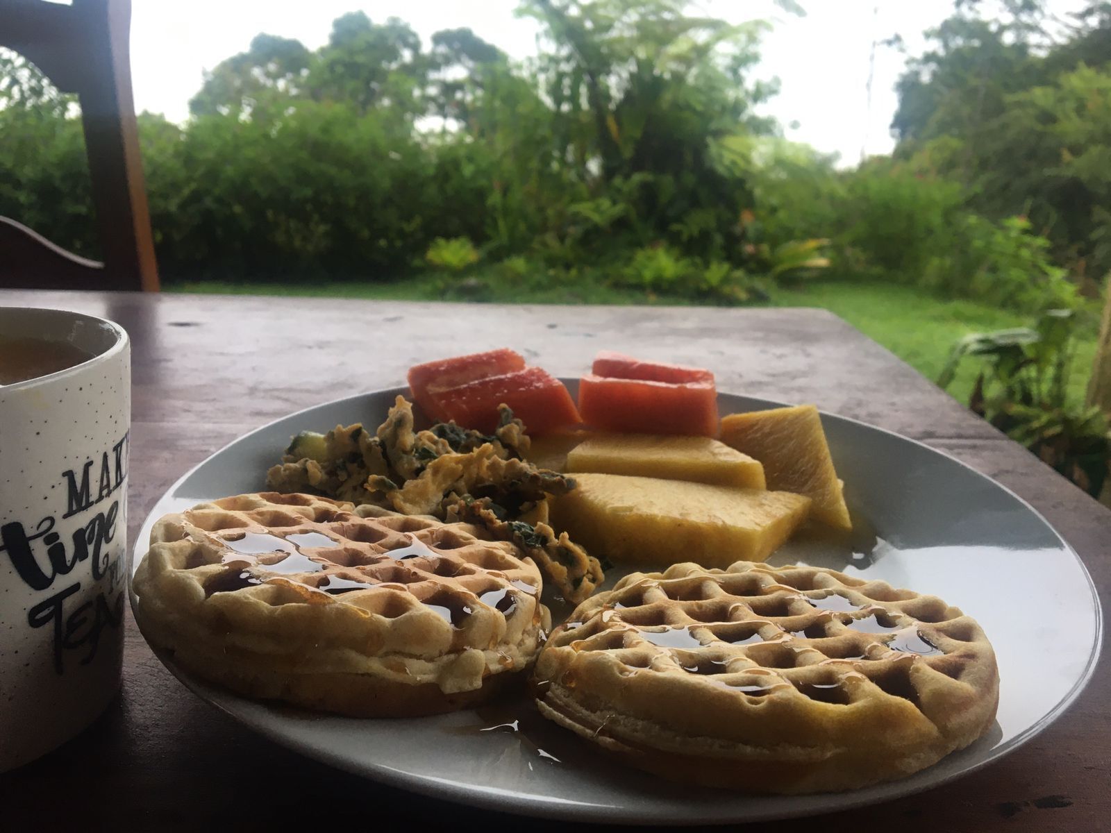 A plate with waffles, a mug, and slices of fruit on a table.