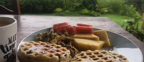 A plate with waffles, a mug, and slices of fruit on a table.