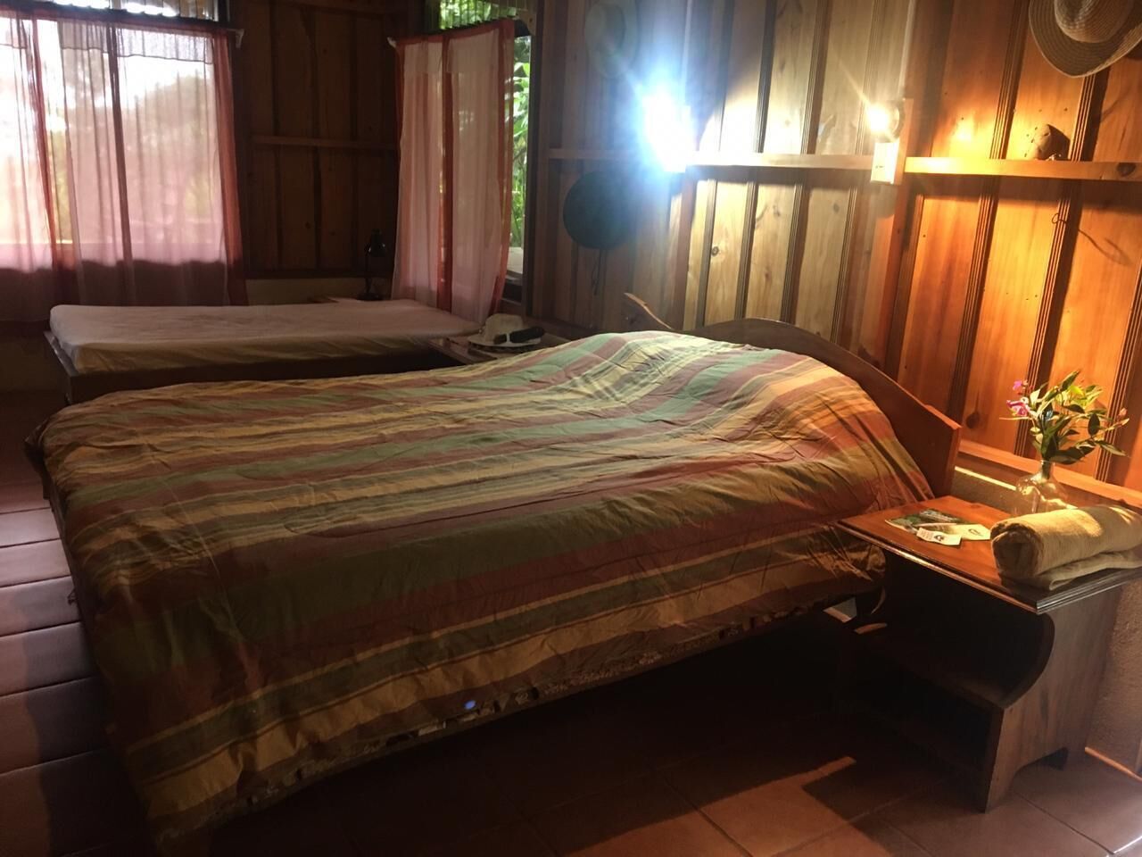 Una habitación con dos camas, una mesita de noche con lámpara y una ventana con cortinas.