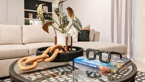 A living room with a sofa, a coffee table with a book and glasses, a plant, and a decorative rope.