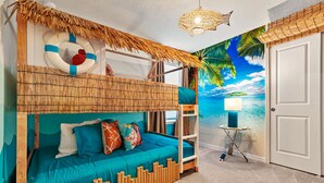 A room with a bunk bed, a beach-themed mural, a hanging light fixture, and a small table with a lamp.