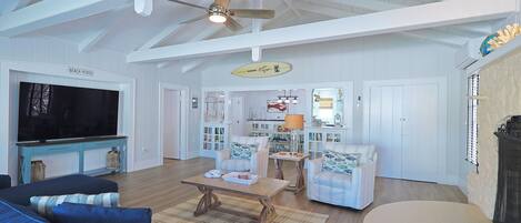 A spacious living room with a large TV, comfortable seating, and a ceiling fan.