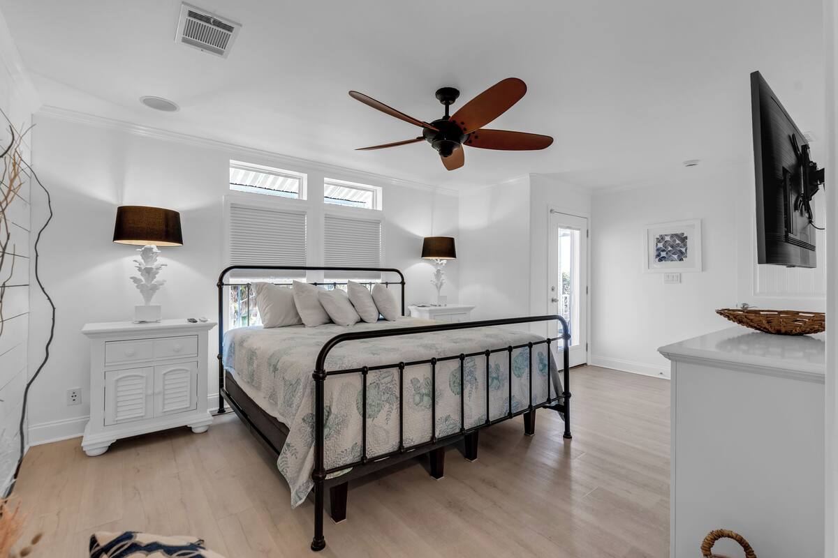 A bedroom with a bed, ceiling fan, bedside lamps, a nightstand, and a dresser.