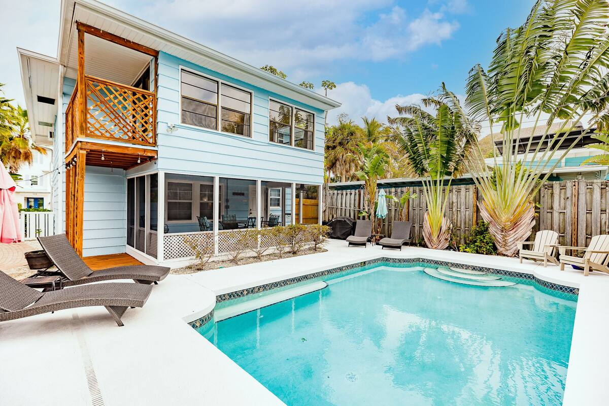A two-story house with a swimming pool, outdoor furniture, and a wooden deck.