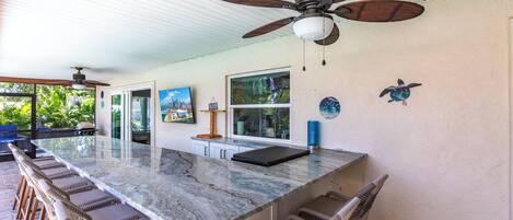 A spacious kitchen with a large island, bar stools, and a ceiling fan.