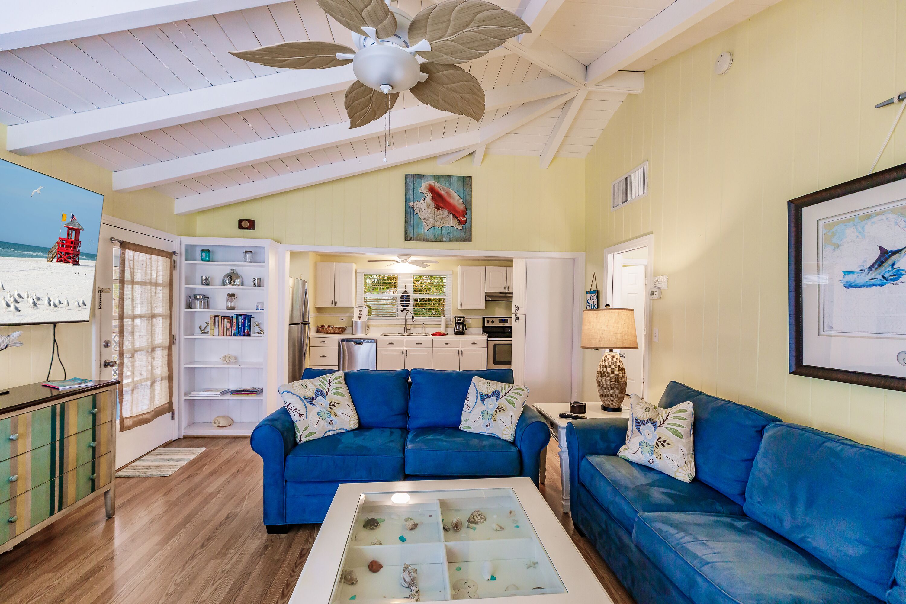 Un salon avec un canapé bleu, une table basse en verre et un ventilateur de plafond.