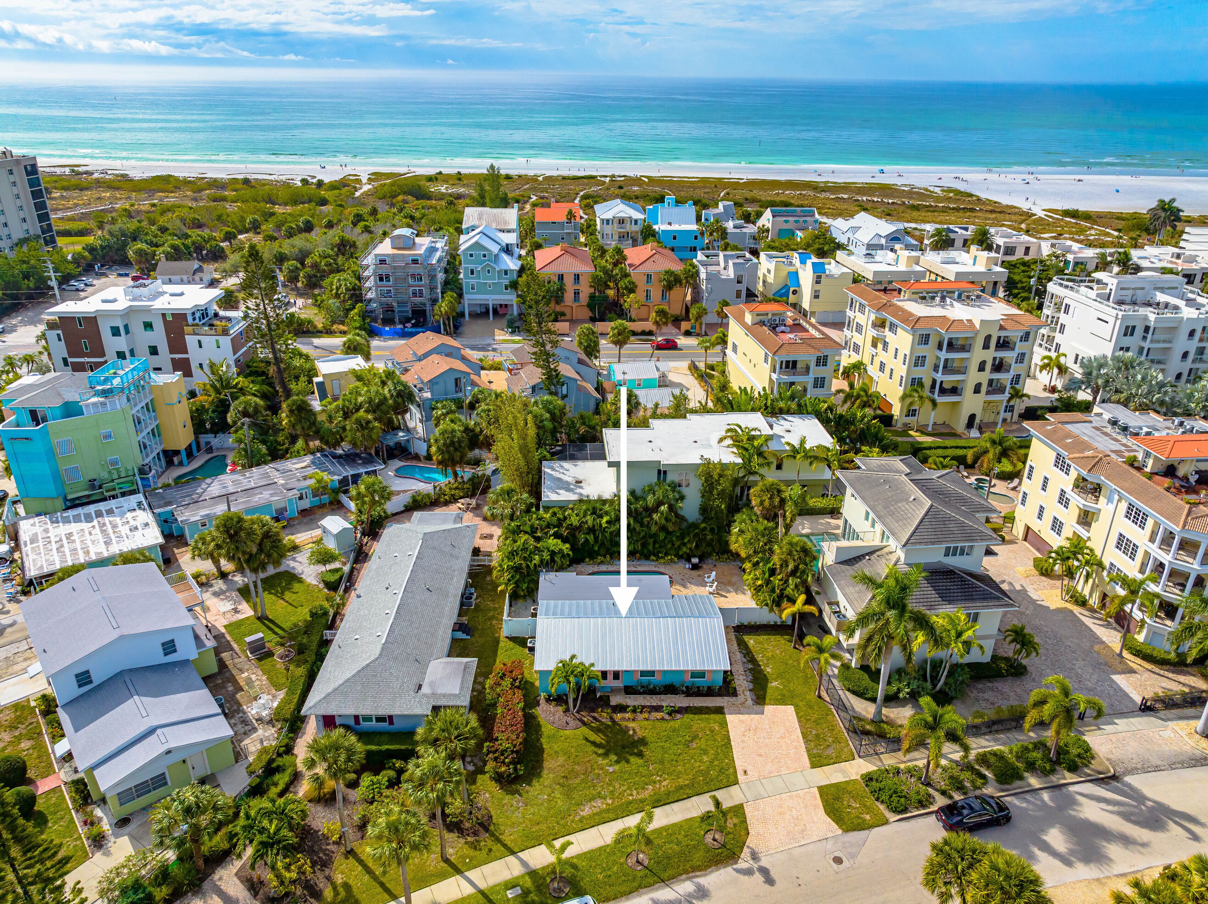 An aerial view of a coastal residential area with colorful buildings, a swimming pool, and a beach in the background.