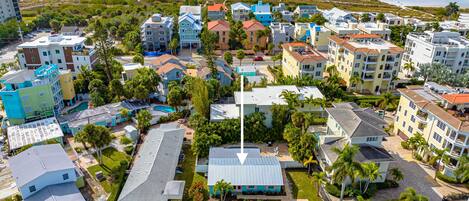 An aerial view of a coastal residential area with colorful buildings, a swimming pool, and a beach in the background.