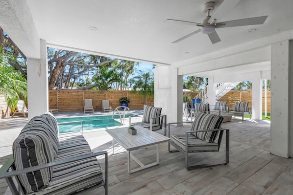 An outdoor patio with a pool, seating, and a ceiling fan.