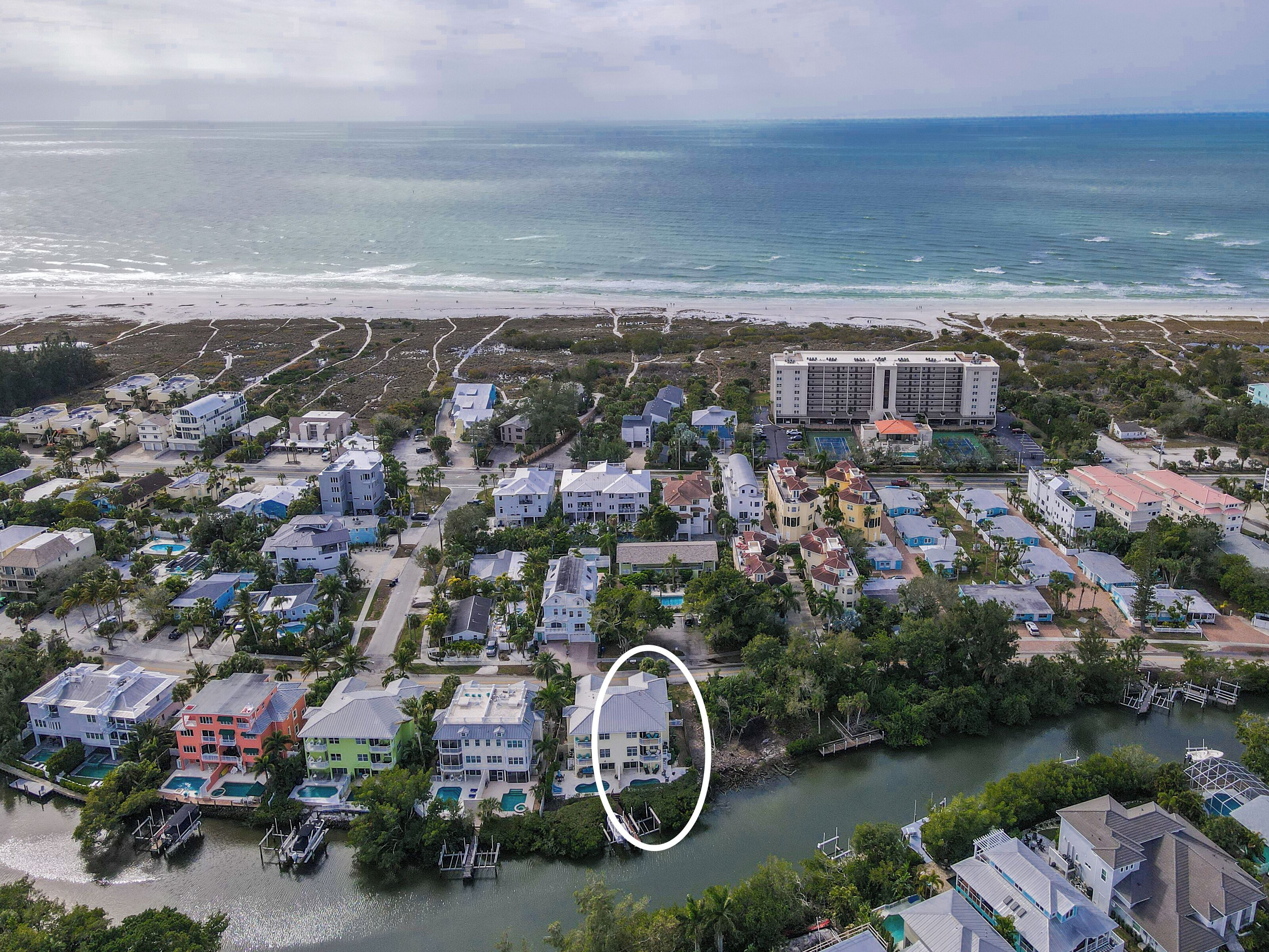 An aerial view of a coastal residential area with houses, a large hotel, and a marina.