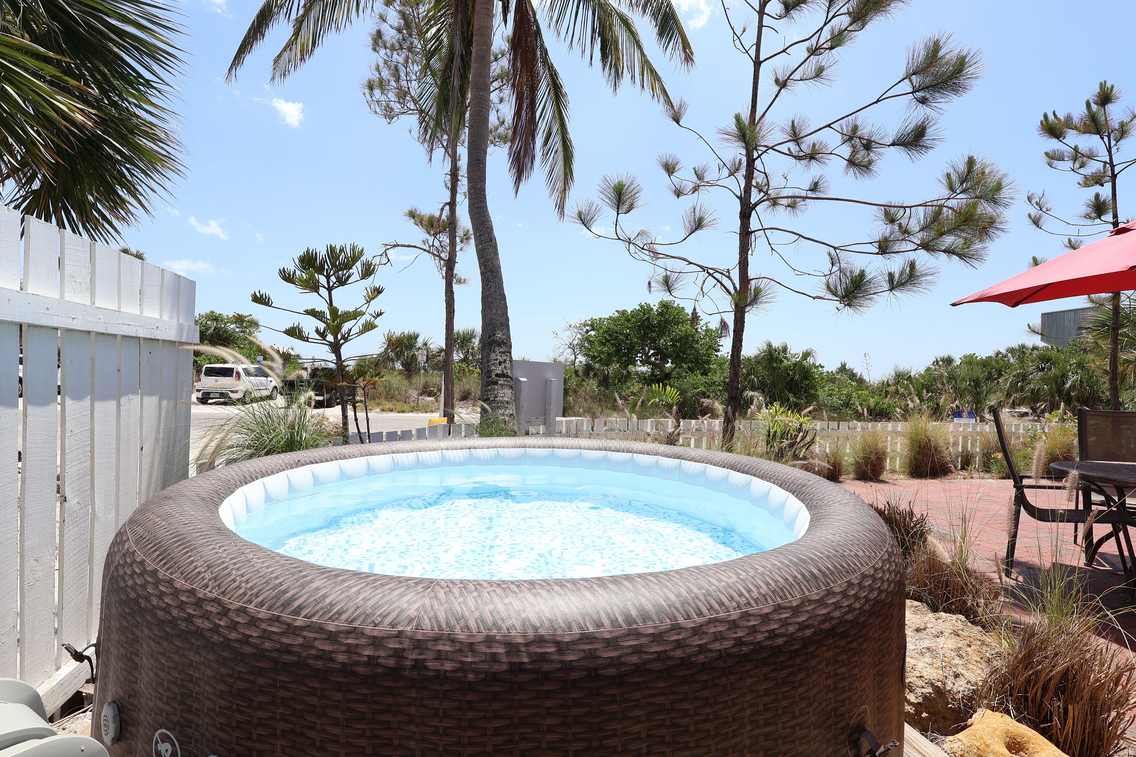 An outdoor hot tub surrounded by palm trees and a wooden fence.