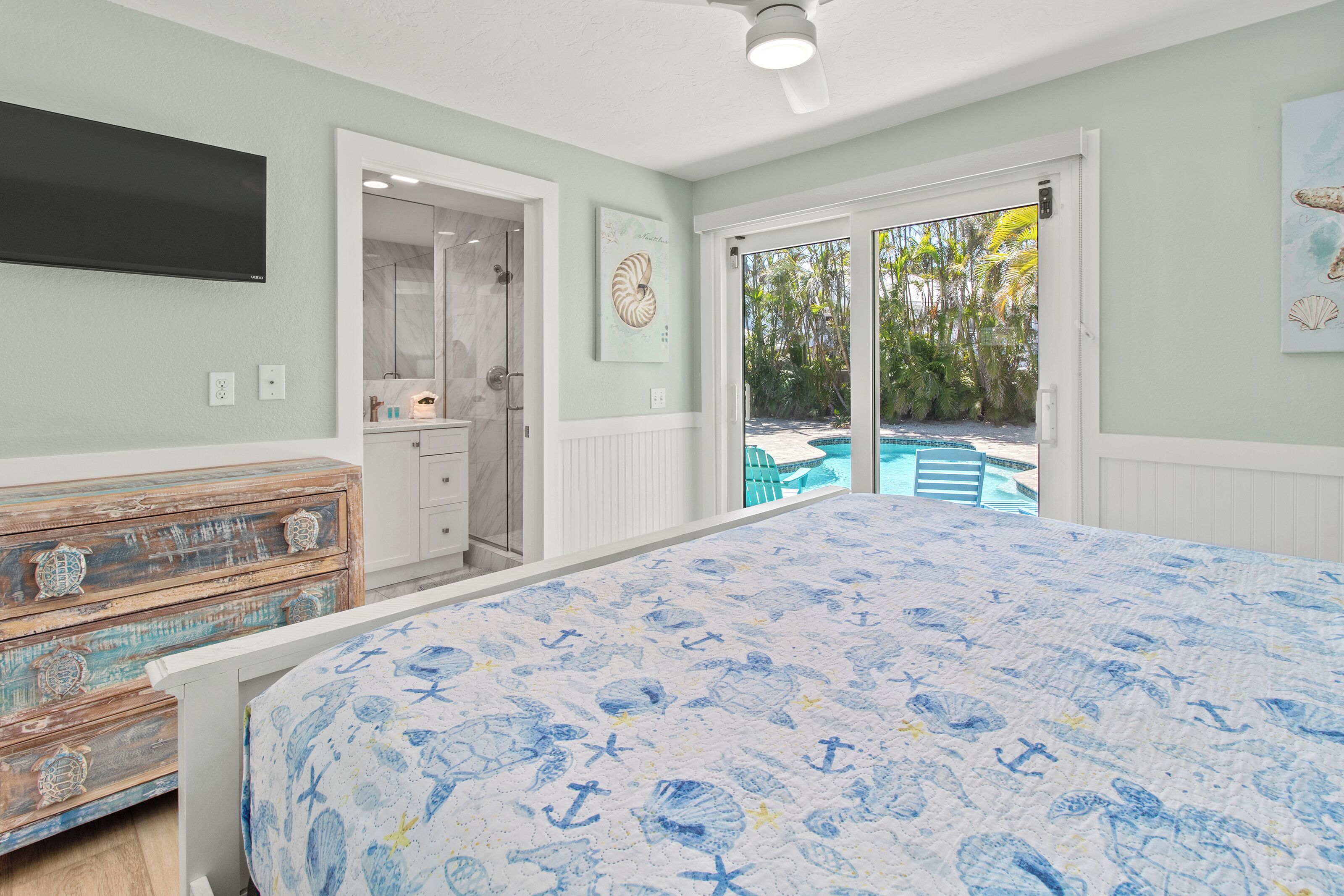 A bedroom with a bed, a dresser, a TV, and a door leading to a pool area.