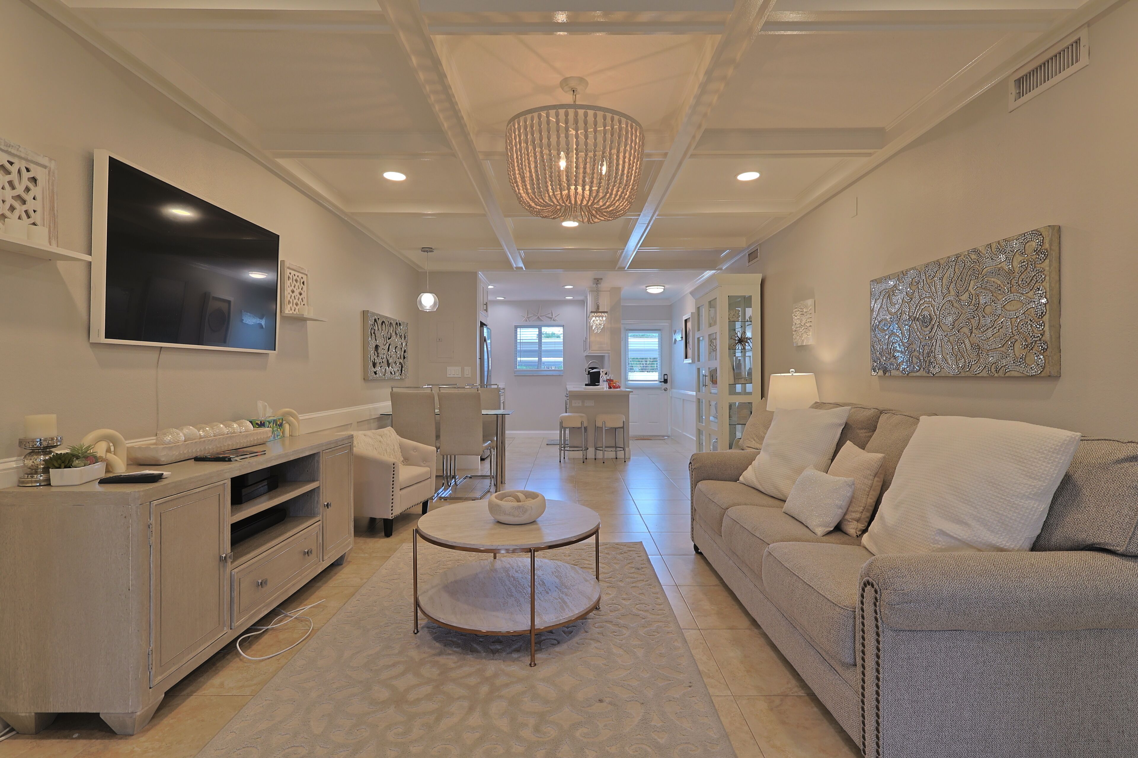 A modern living room with a flat-screen TV, a chandelier, and a sofa.