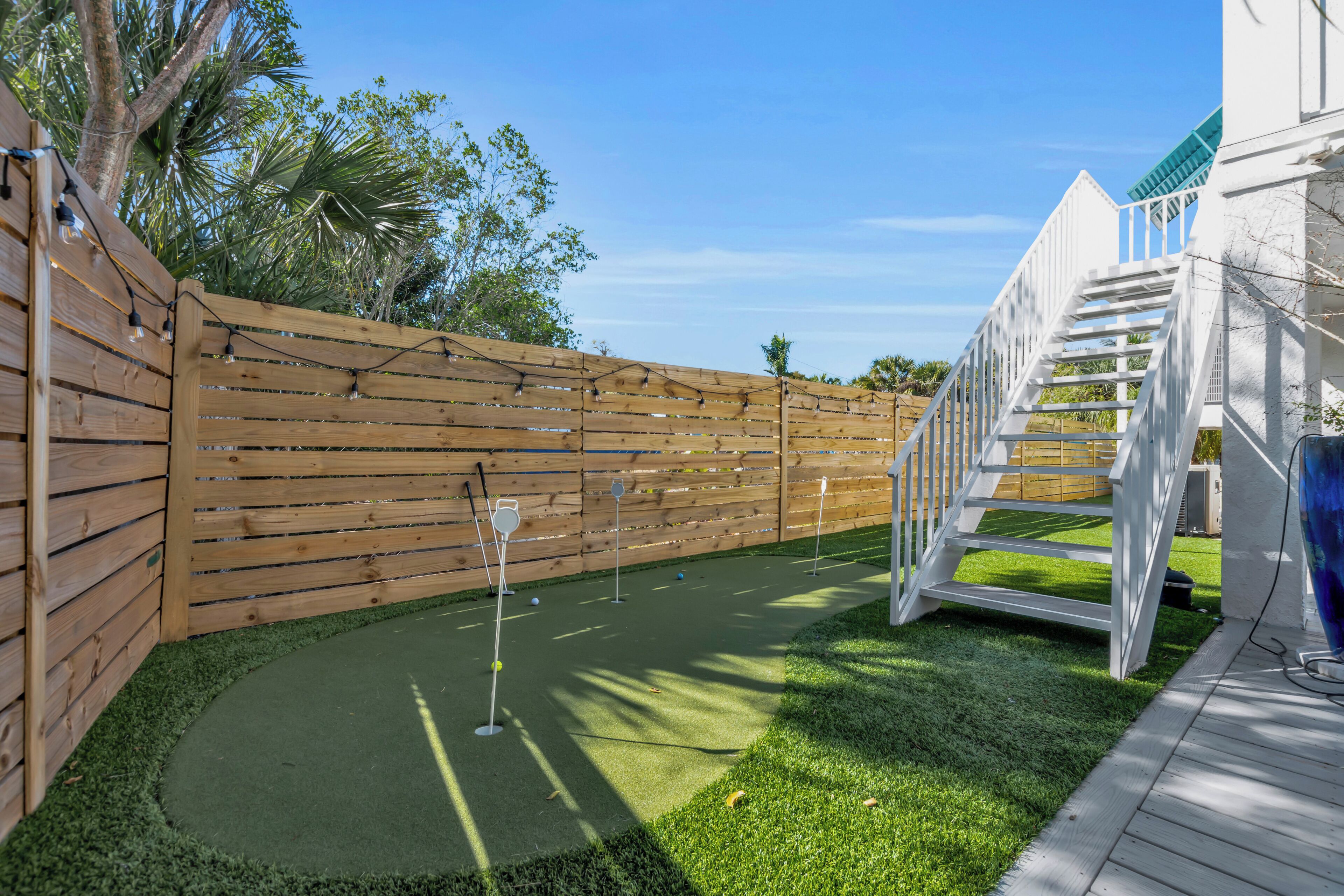 A miniature golf course with a wooden fence, a white staircase, and a clear sky.