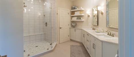 Un baño moderno con ducha envuelta en vidrio, muebles de color blanco y un espejo grande.