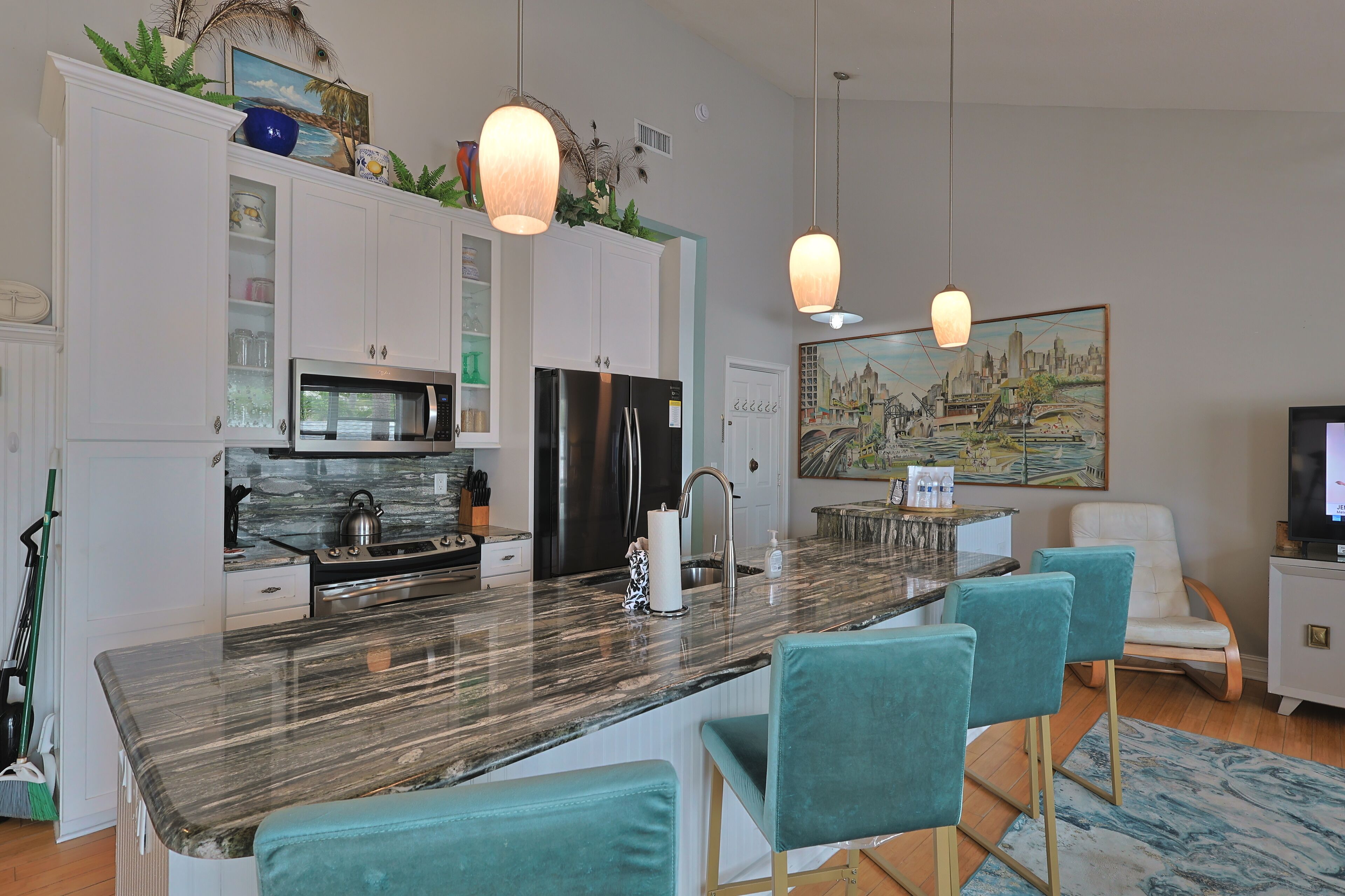 A modern kitchen with a marble countertop, stainless steel appliances, and teal bar stools.