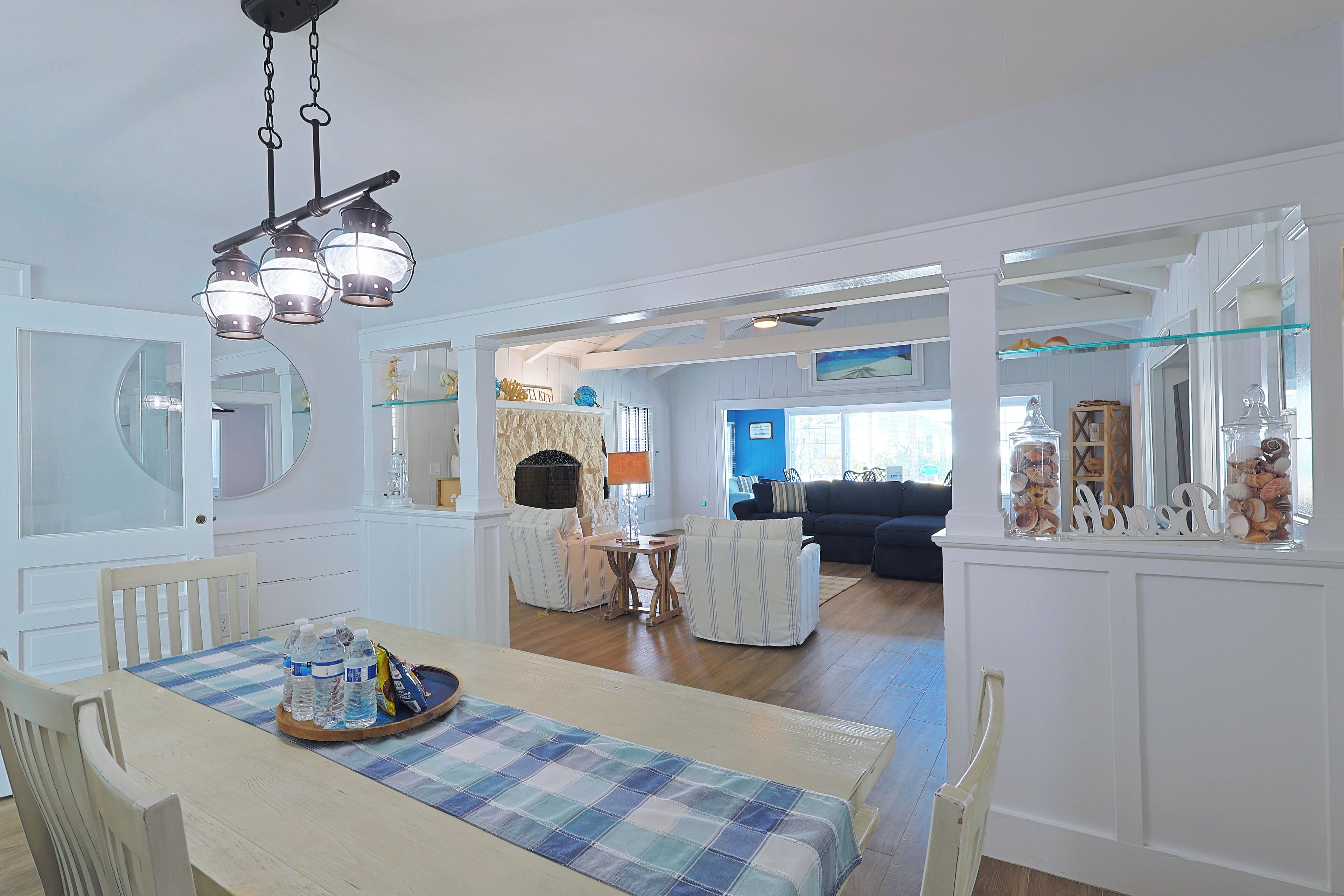 Uma sala de jantar com uma mesa posta para quatro pessoas, um candelabro e vista para uma sala de estar com parede azul.