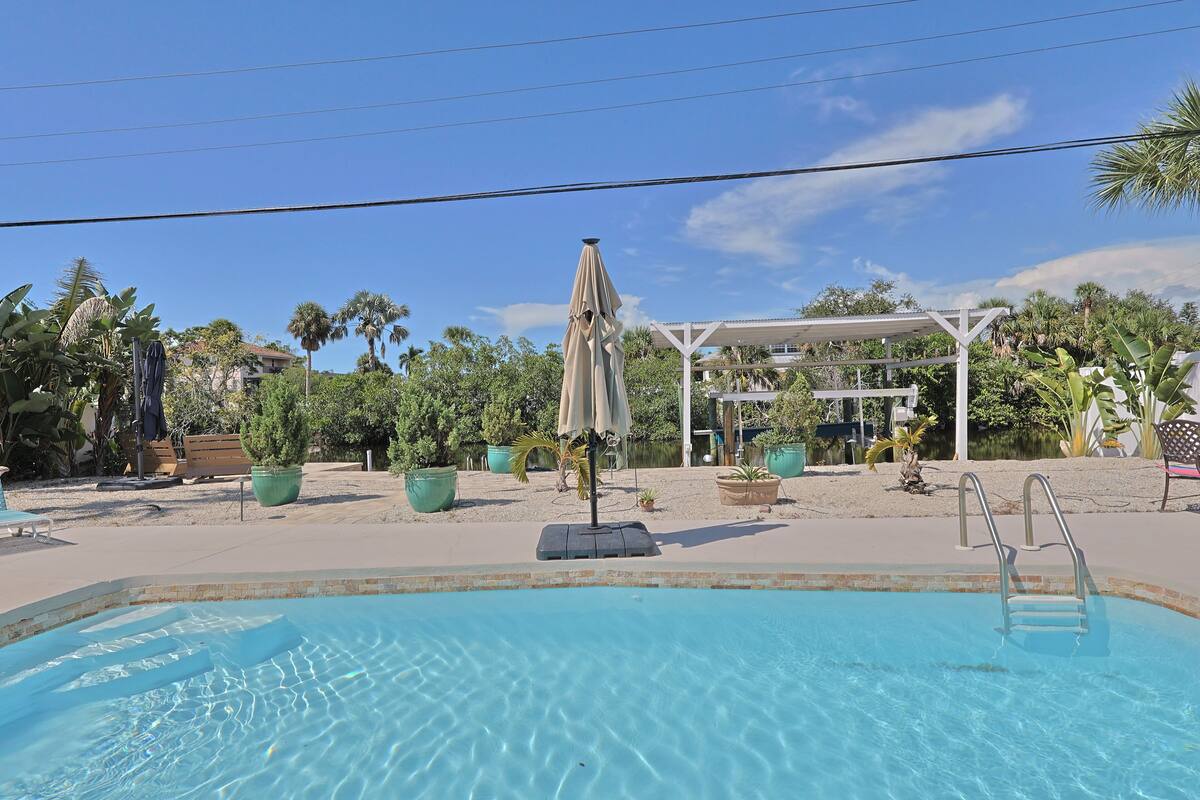 A swimming pool with a lifeguard chair, a shaded area, and a white pergola in the background.