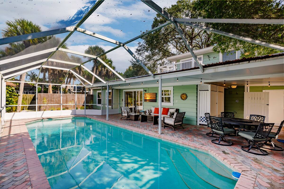 A covered outdoor swimming pool with a patio area, including seating and a table.