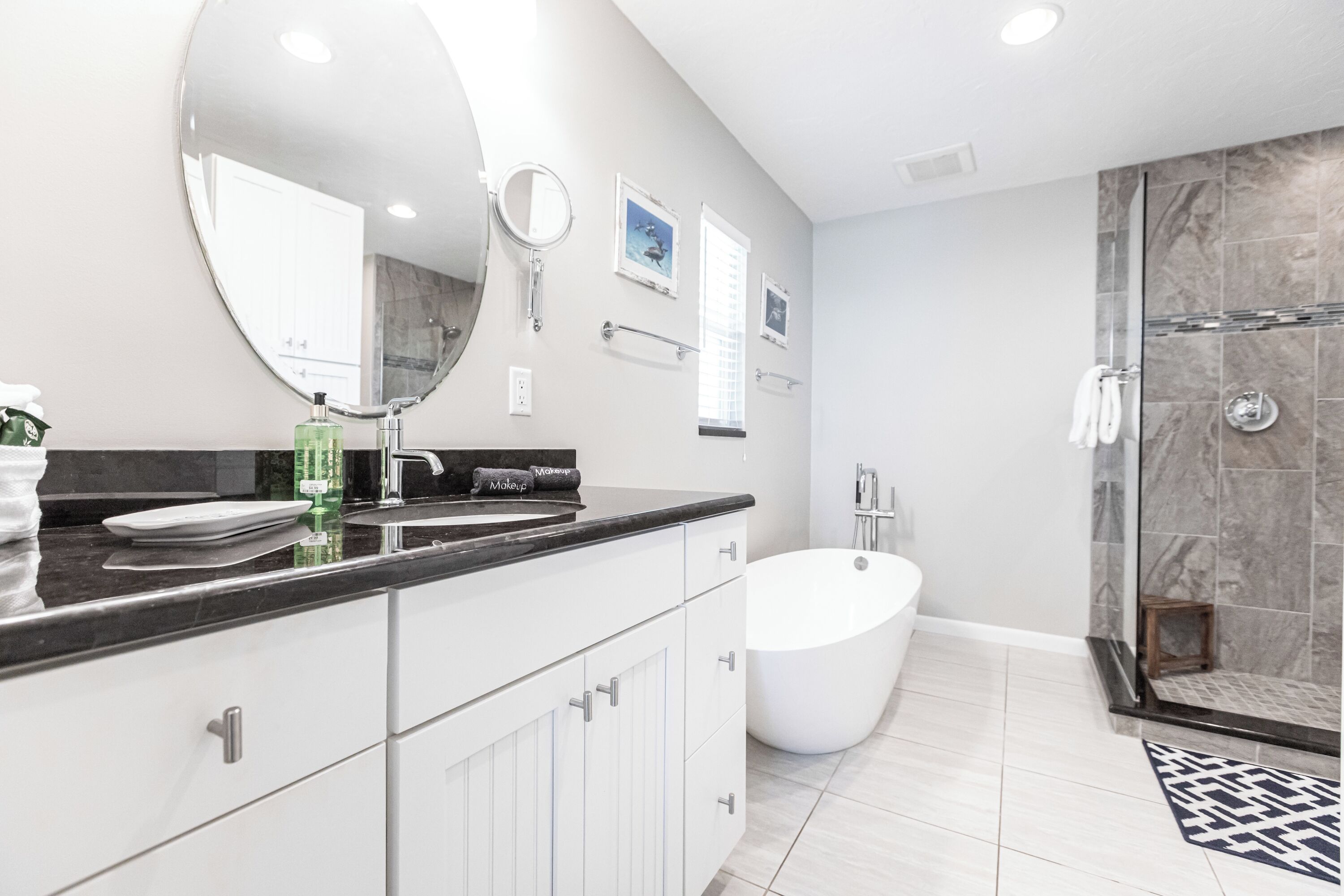 A modern bathroom with a large mirror, two sinks, a bathtub, and a shower area.