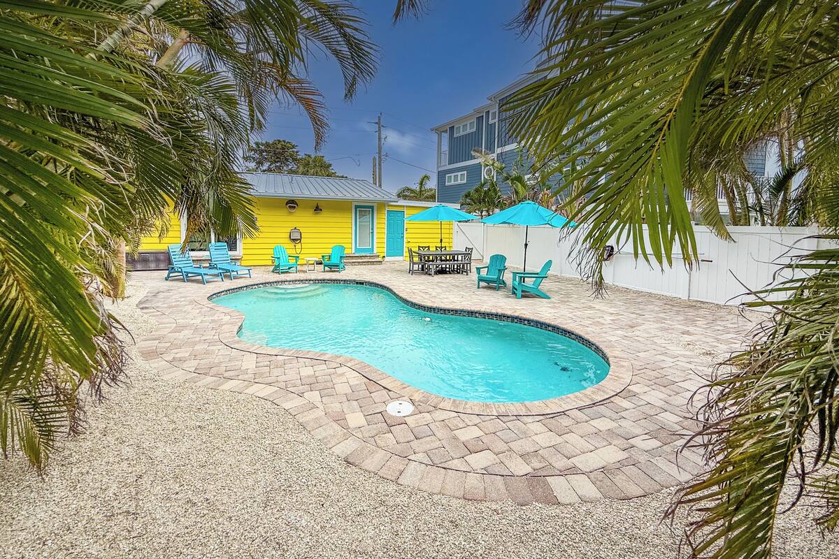 A swimming pool surrounded by blue chairs and a yellow building.