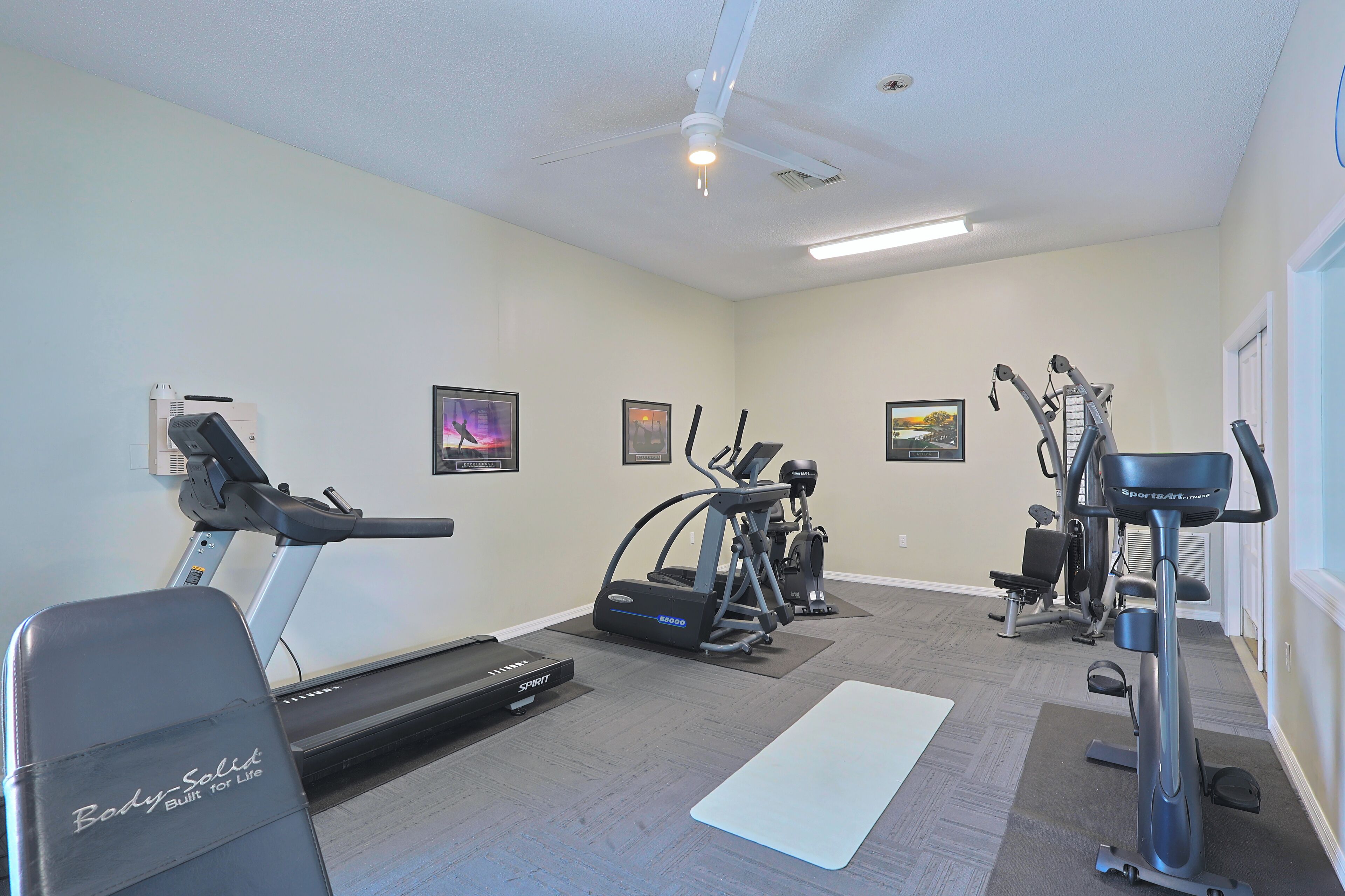 A home gym with a treadmill, elliptical, stationary bike, and a yoga mat.