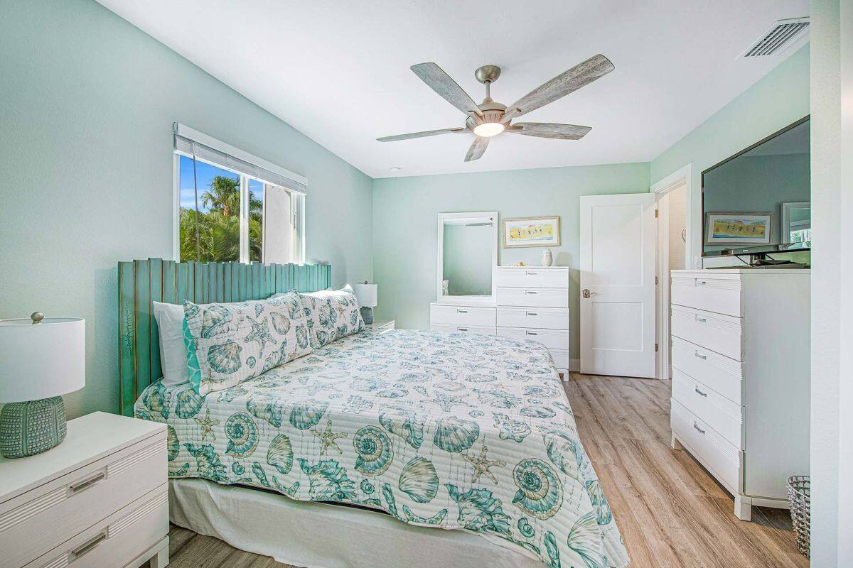 A bedroom with a bed, a ceiling fan, a window, a dresser, and a mirror.