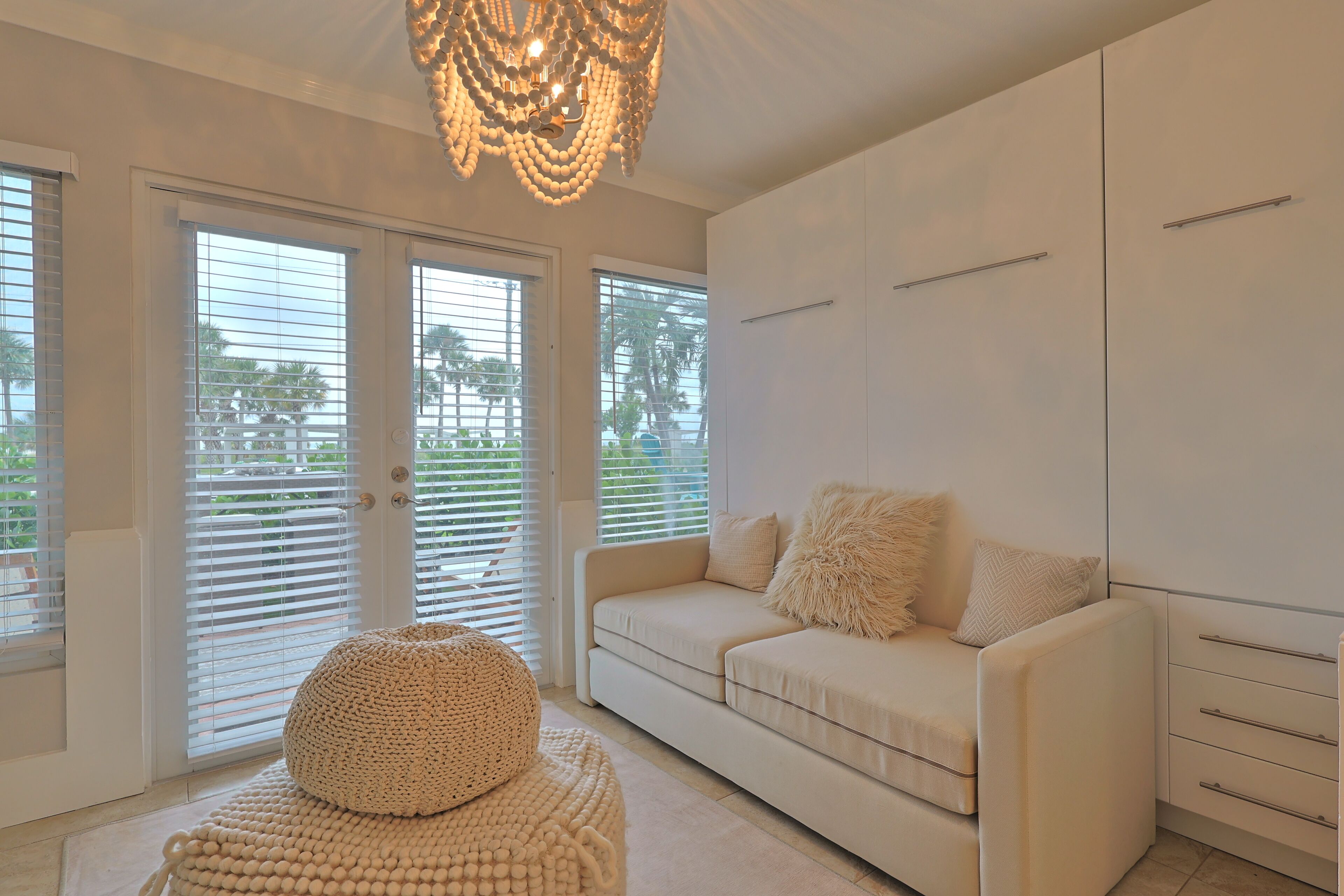 A modern living room with a beige sofa, a round pouf, and a chandelier.