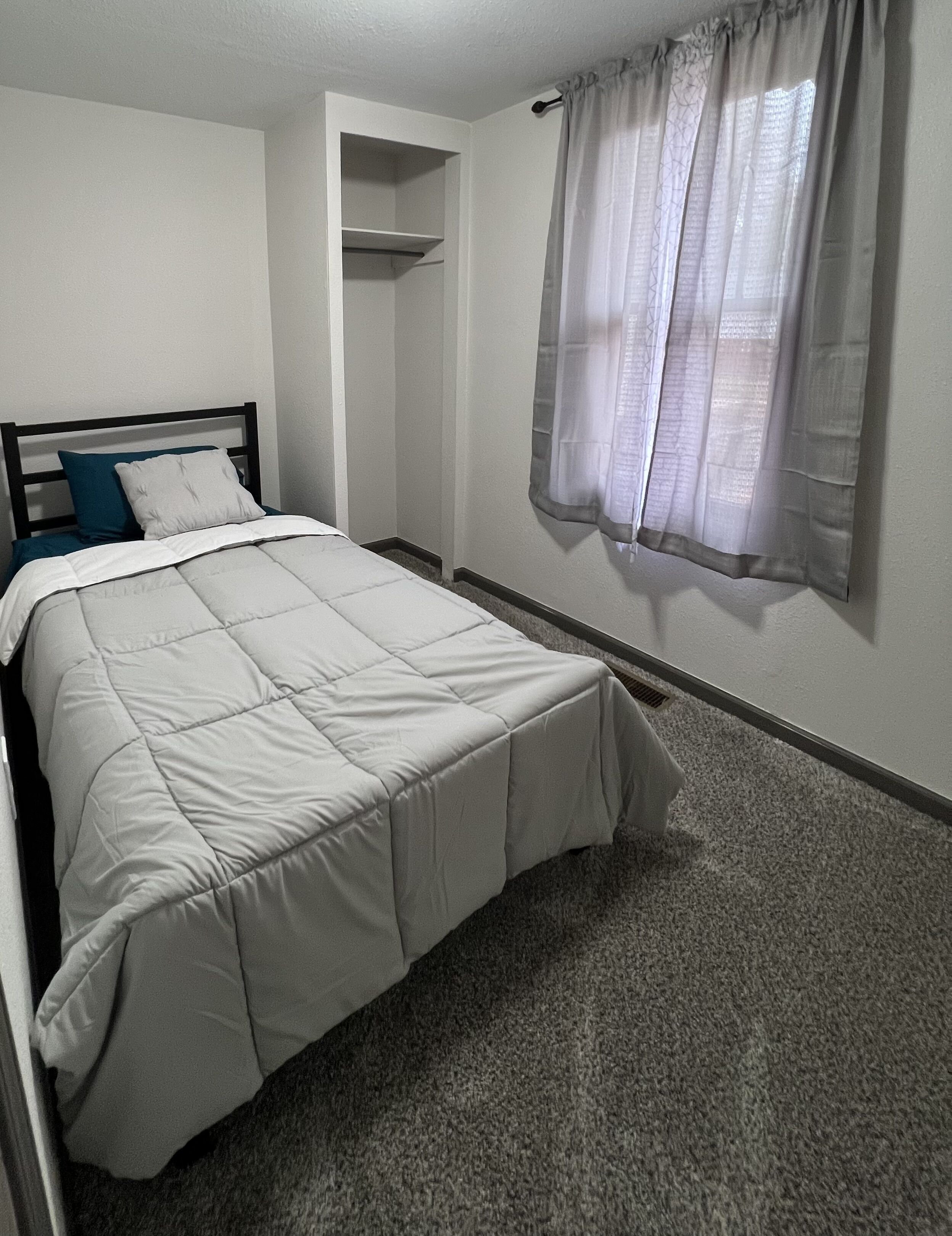 Un dormitorio con cama, vestidor y ventana con cortinas de gasa.