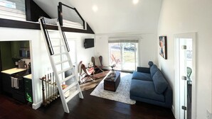 Un vaste espace de vie avec une chambre en mezzanine, un escalier et une vue sur l’extérieur.