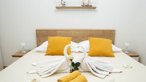 Una cama bien hecha con almohadas blancas y amarillas, una toalla dispuesta en forma de corazón y una rosa.
