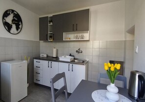 Moderni keittiö, jossa on valkoiset kaapit, maailmankarttakuvioinen seinäkello, pesuallas ja maljakko, jossa on keltaisia kukkia pöydällä.