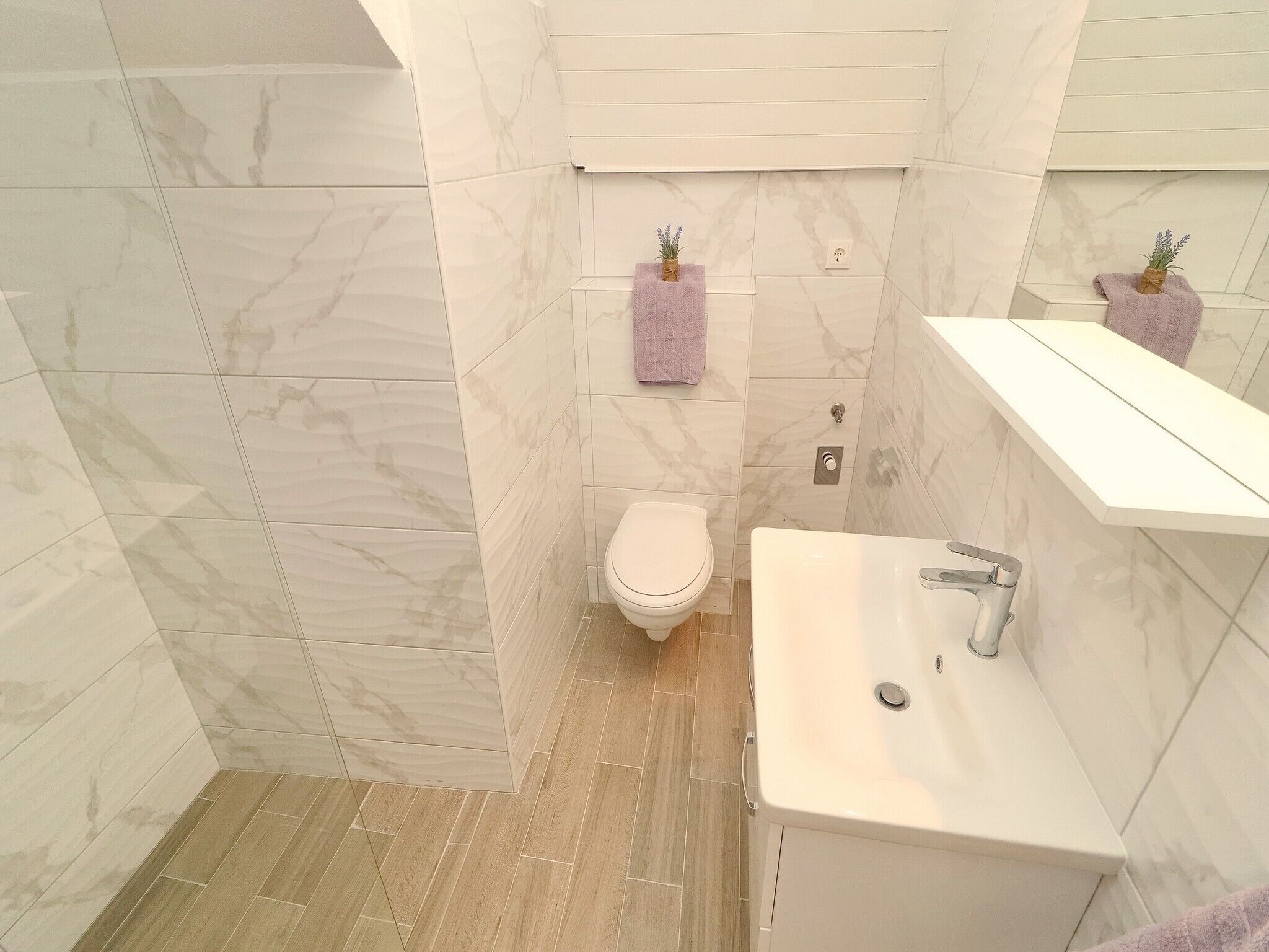 A bathroom with a toilet, sink, and mirror. There are two towels hanging on hooks.