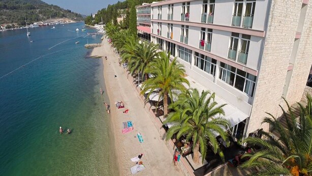Ett hotell vid kusten med utsikt över stranden, flera balkonger och palmer.