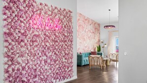 A room with a floral wall, a neon sign, a teal sofa, and a dining area with chairs and a table. - PinkBlissHouz: Pool, Spa, Firepit, Themed Rooms (Desert Hot Springs)