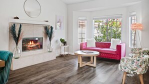 A living room with a fireplace, a pink sofa, and a round coffee table. - PinkBlissHouz: Pool, Spa, Firepit, Themed Rooms (Desert Hot Springs)