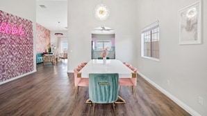 A modern dining area with a white table, pink upholstered chairs, and a teal accent chair. - PinkBlissHouz: Pool, Spa, Firepit, Themed Rooms (Desert Hot Springs)