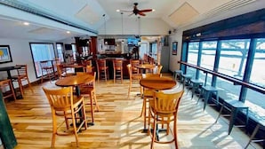 A spacious indoor area with wooden flooring, multiple tables and chairs, a central bar area, and large windows providing natural light. - *Posh 2BR in the Heart of the Pittsford Village* (Pittsford)