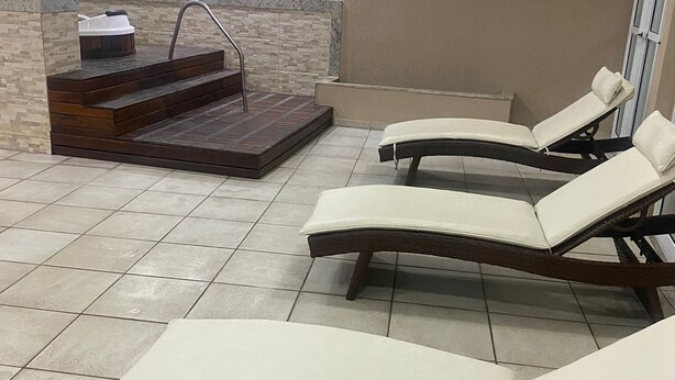 A spa area with three reclining chairs, a stone wall, and a small pool with steps leading up to it.