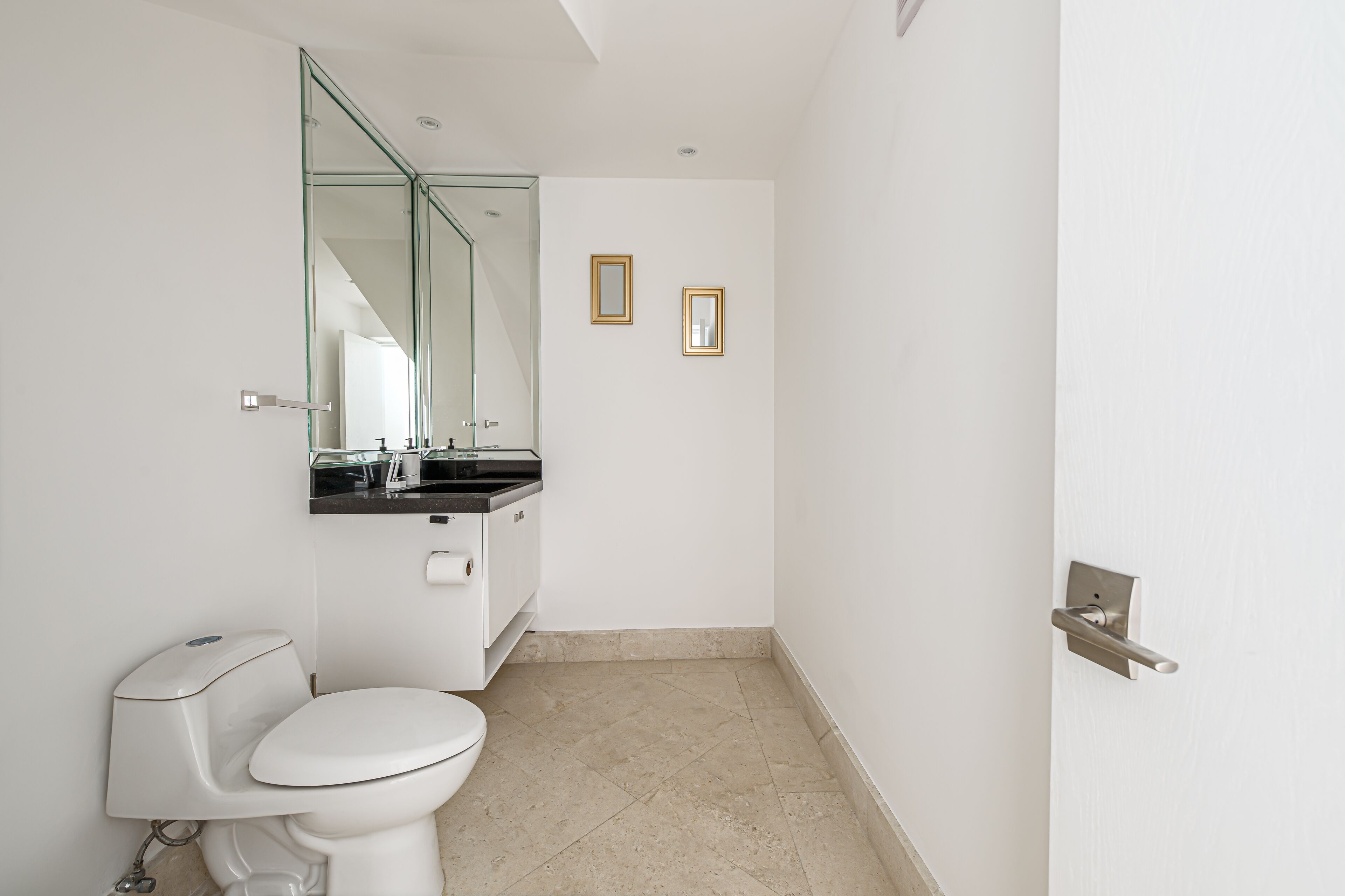 A modern bathroom with a toilet, a sink, and a mirror. There are two framed pictures on the wall.