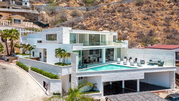 A modern two-story house with a swimming pool, a stone pathway, and a hillside backdrop.