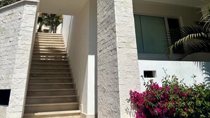 A modern building with a staircase leading to an upper level, surrounded by palm trees and a balcony with a glass railing.
