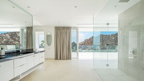 A modern bathroom with a large mirror, a glass shower enclosure, and a view of rocky terrain.